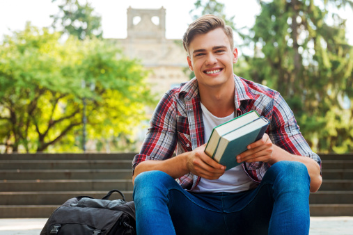 Smiling male student in red t-shirt holding books and looking at the camera