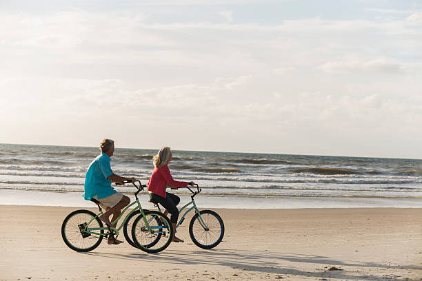 matura coppia con biciclette in spiaggia - mature adult bicycle senior adult heterosexual couple foto e immagini stock