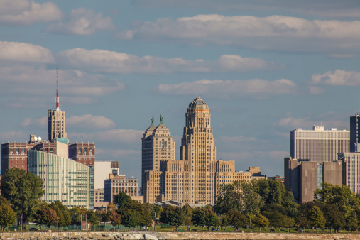 A view of downtown Buffalo from Ft. Erie near the Peace Bridge.  City Hall, Liberty Bank, M&T Bank, Federal Court and other buildings. Blue sky white clouds, trees along river bank