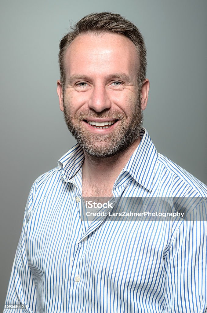 Portrait of a smiling happy handsome man Portrait of a smiling happy handsome middle-aged man with a beard wearing a striped shirt looking at the camera with a warm friendly smile against a grey studio background Adult Stock Photo