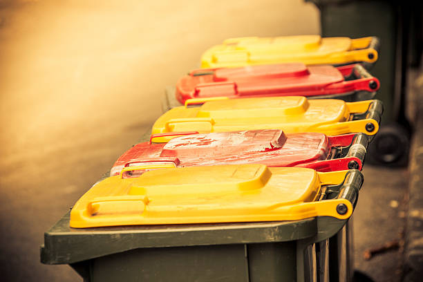 Ready for the garbos: yellow and red-topped garbage bins in alternating colours outside in a residential back alley. Closed (lids down), Selective focus (on second bin), horizontal, copy space, some noise for effect.