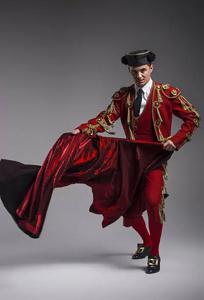 Studio shot of man dressed as Spanish torero, matador, bullfighter. Performing a traditional classic bullfight, standing and holding the capote.