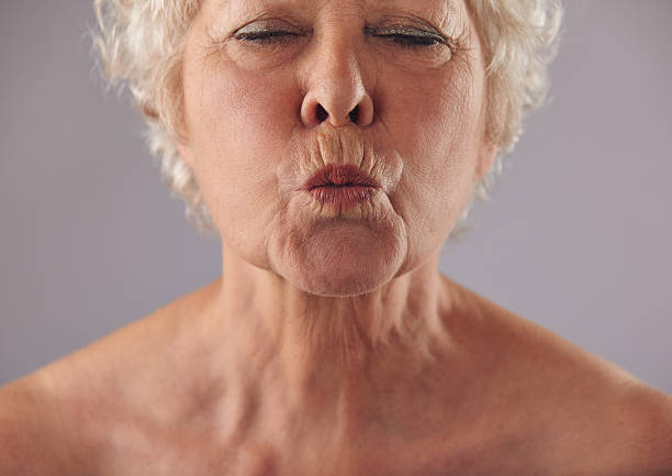 Senior woman puckering lips Cropped portrait of senior woman puckering lips. Mature female grimacing against grey background mouths kissing stock pictures, royalty-free photos & images