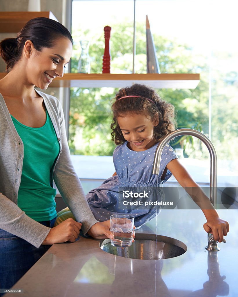 Everyone needs a kitchen helper Shot of a little girl helping her mother fill a glass with water in the kitchen Water Stock Photo