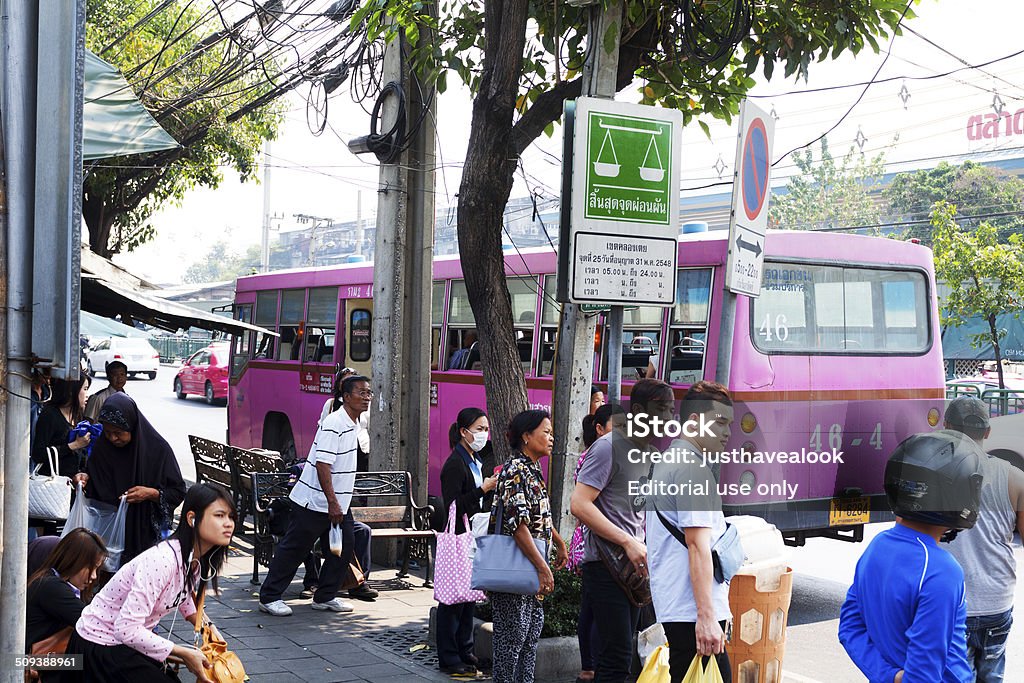 Thai people at bus stop Bangkok, Thailand - February 3, 2014: Capture of Thai people at bus stop on street Rama IV Road. People are looking and waiting for next bus. A woman is wearing a surgical mask. In background a pink bus out of order is standing. Adult Stock Photo