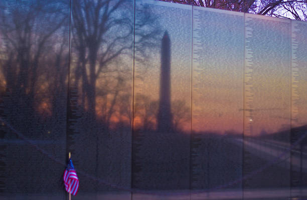 Washington, D.C. USA - January 31, 2014: Reflection of the Washington Monument in the Vietnam Memorial Wall at sunrise, with a flag against the wall