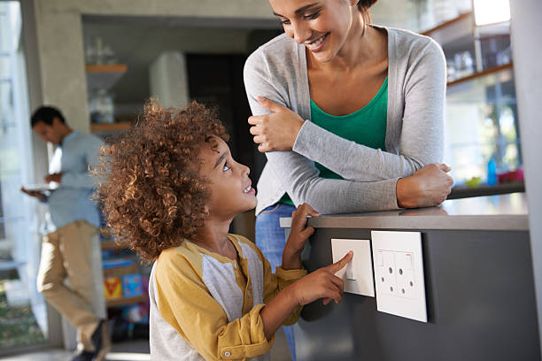 Solving the energy crisis one switch at a time Shot of a little boy turning off an electrical switch while his mother looks on electrical safety at home stock pictures, royalty-free photos & images