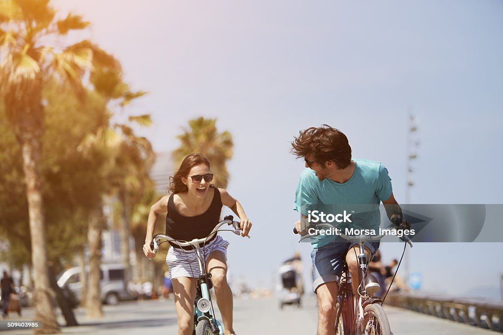 Woman chasing man while riding bicycle Happy young woman chasing man while riding bicycle during summer vacation Summer Stock Photo