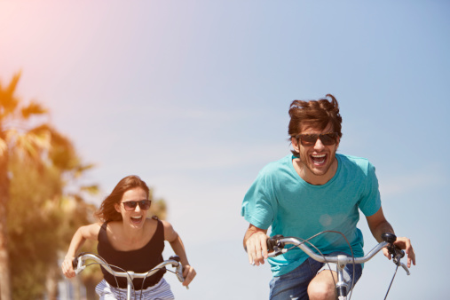 Happy young woman chasing man while riding bicycle during summer vacation