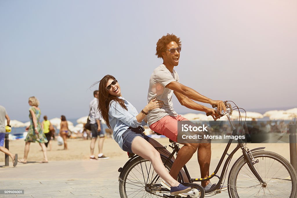 Couple riding bicycle at beach Side view of multi-ethnic couple riding bicycle at beach Beach Stock Photo