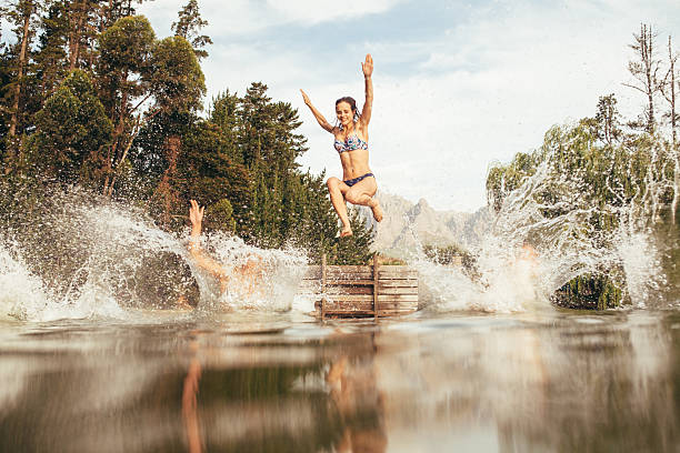 Women jumping into a lake from jetty Portrait of young women jumping into a wilderness lake from the jetty. Young girl jumping from a pier at the lake jumping into water stock pictures, royalty-free photos & images