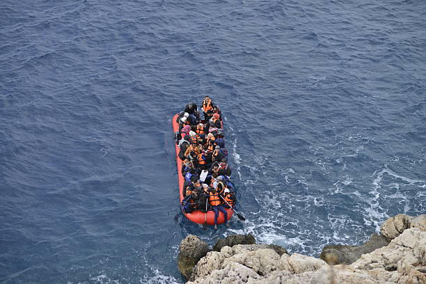Migrants Kas,Turkey - January 16, 2016, Coast line between Kalkan Kas at 09:45. An inflatable boat filled with refugees and other migrants approaches the south coast of the Turkey. Picture captured from Kalkan Kas Road D400.   immigrant stock pictures, royalty-free photos & images