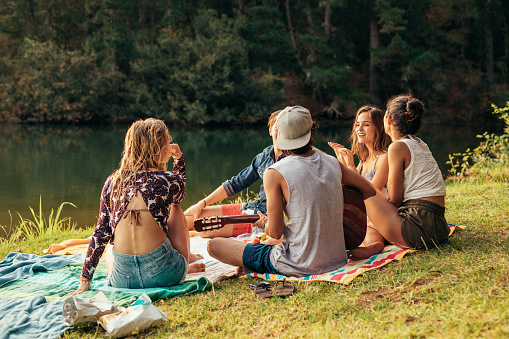Young people having picnic near a lake. Young friends relaxing by a lake.
