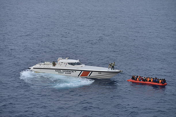 Turkish coast guard boat approaches an overcrowded inflatable raft carrying migrants at sea.
