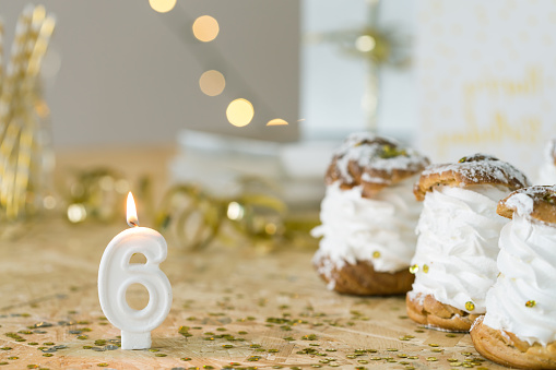 Number six birthday candle and three cream puffs on decorated gold table