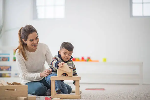 A mother and her toddler son are playing together in their home on mother's day. The little boy is building a block tower.
