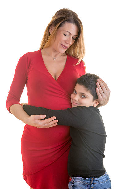 Portrait of beautiful pregnant mother with his older son holding her tummy, smiling and happy against isolated white background.
