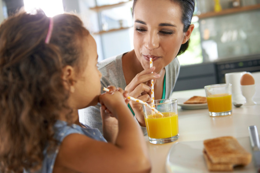 Shot of a young mother and daughter sharing a glass of orange juice at breakfast