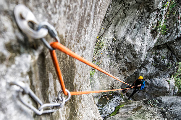 Rappeling in the canyon Member of canyoning team with yellow protective helmet moving down the stream in the canyon. Rope security system is in front. carabiner stock pictures, royalty-free photos & images