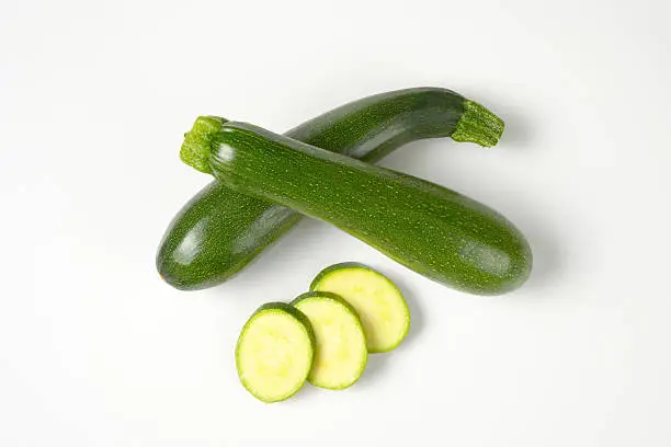 whole courgettes and courgette slices on white background