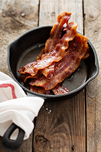Sizzling hot bacon pieces in a cast iron skillet