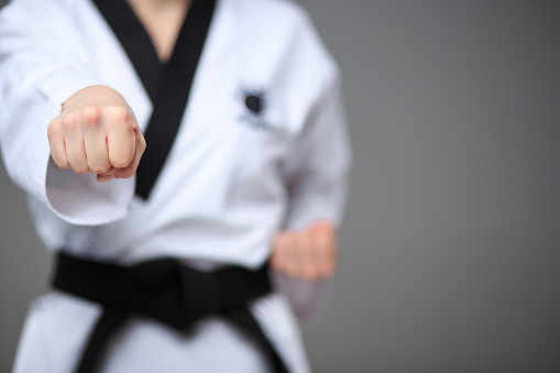 The hand of karate girl in white kimono and black belt training karate over gray background.