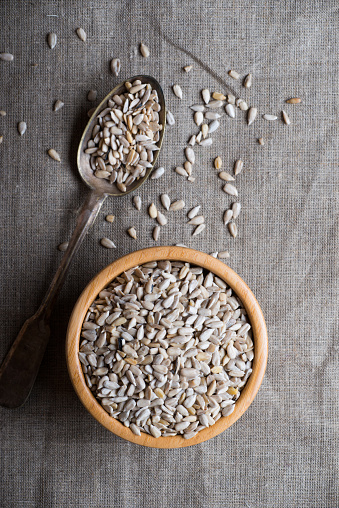 Raw peeled sunflower seeds in wooden bowl over linen napkin