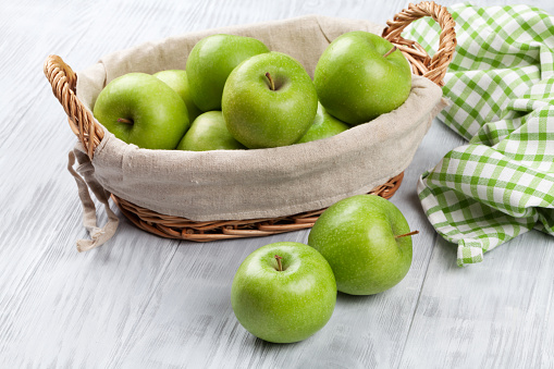 Green apples in basket over wooden table