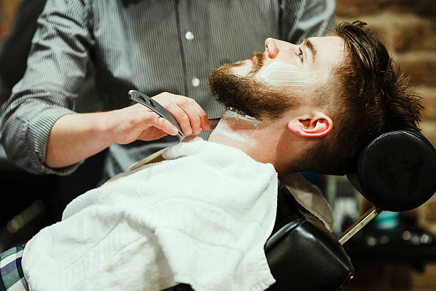 Barber shaving a bearded man stock photo