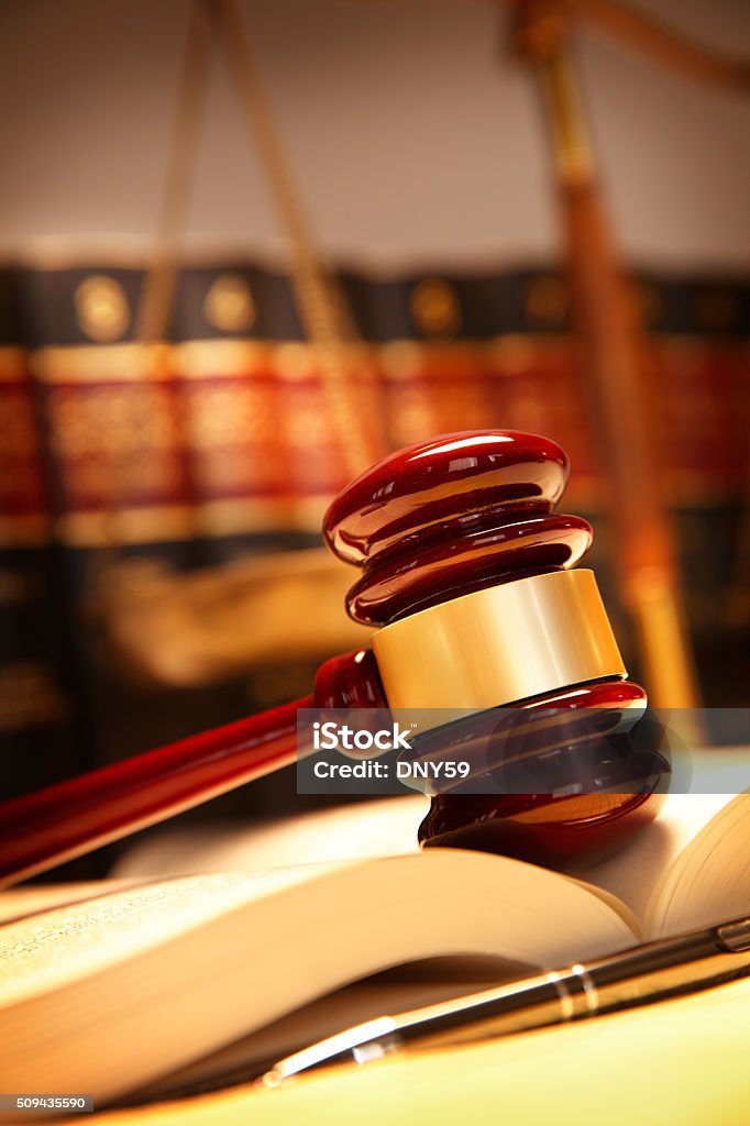 Gavel Resting On Top Of Open Law Book A wooden gavel rests on top of an open law book in front of a row of law books and a justice scale that are out of focus in the background.  A ballpoint pen sits on a legal pad in the foreground. Photographed using a shallow depth of field. Equal-Arm Balance Stock Photo