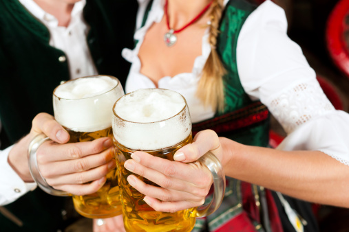 Young couple, man and woman, in traditional Bavarian Tracht drinking beer in a brewery in front of beer barrels
