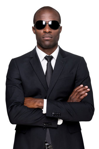 Serious young African man in formalwear and sunglasses keeping arms crossed and looking at camera while standing isolated on white background
