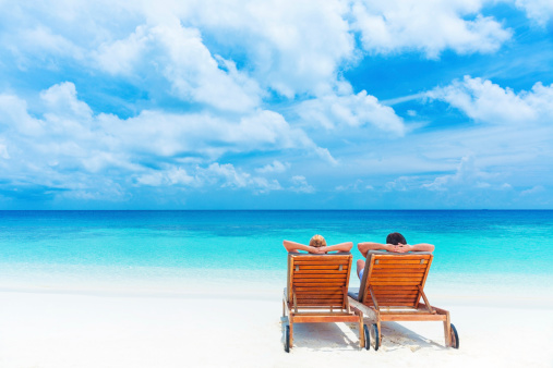 Two happy people relaxing on the beach, sitting down on comfortable sunbed and taking sunbath, rear view, summer holidays concept