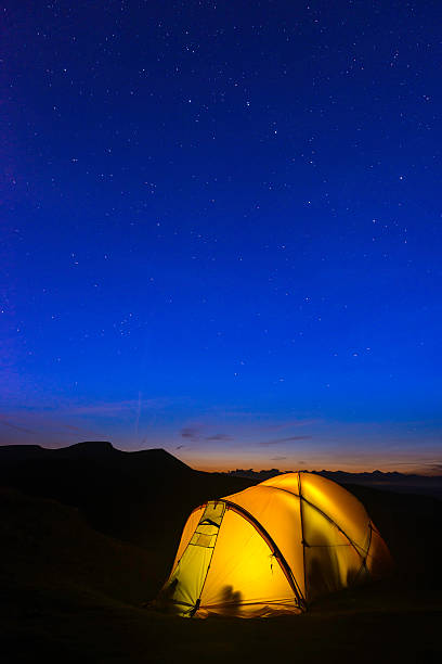istock Stars shining over warm glowing tent and silhouetted mountain peaks 509442341