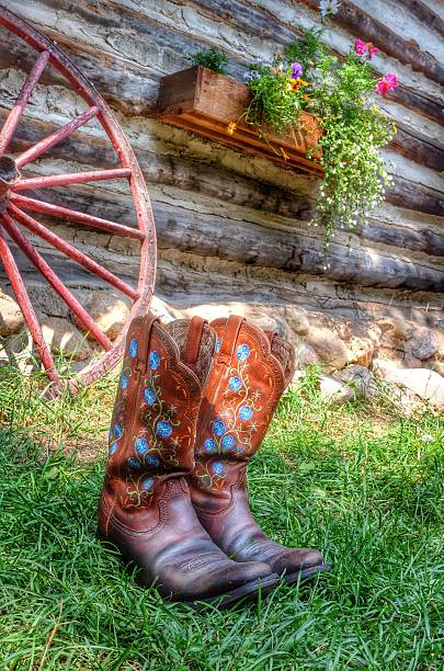 Old, worn leather boots placed on a wooden shelf. The boots are brown and show signs of age and use, surrounded by rustic wooden tools.