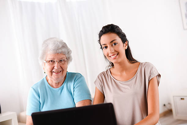 istock cheerful young woman teaching computer and internet to elderly person 509446455