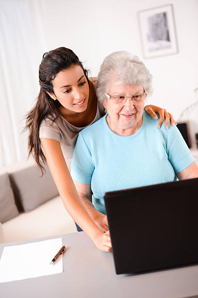istock cheerful young woman teaching computer and internet to elderly person 509446863