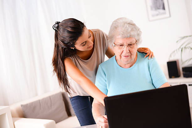 istock cheerful young woman teaching computer and internet to elderly person 509464333