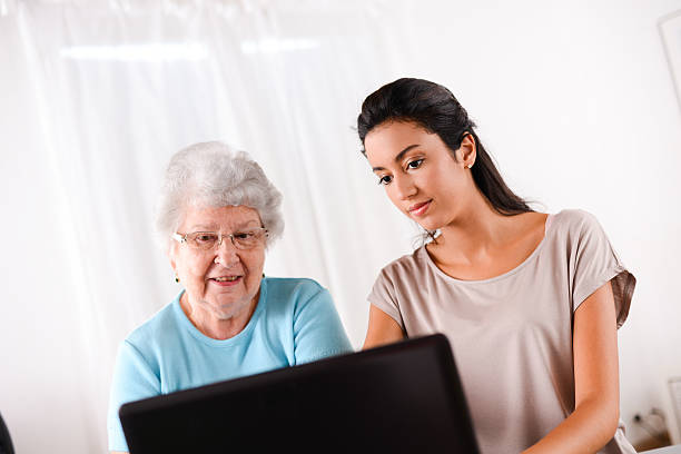istock cheerful young woman teaching computer and internet to elderly person 509464855