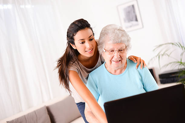 istock cheerful young woman teaching computer and internet to elderly person 509464857