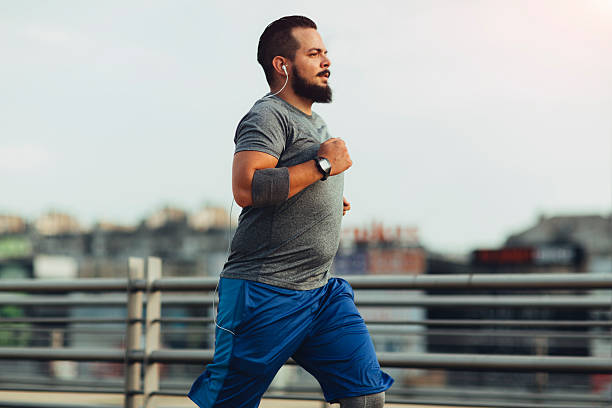 Get fit in the city Urban hipster man running in the city. He is listening music and trying to get fit. Buildings in background. Wearing modern sports clothes. overweight stock pictures, royalty-free photos & images