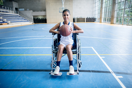 Disabled woman playing basket sitting on a wheelchair and looking at camera holding the ball