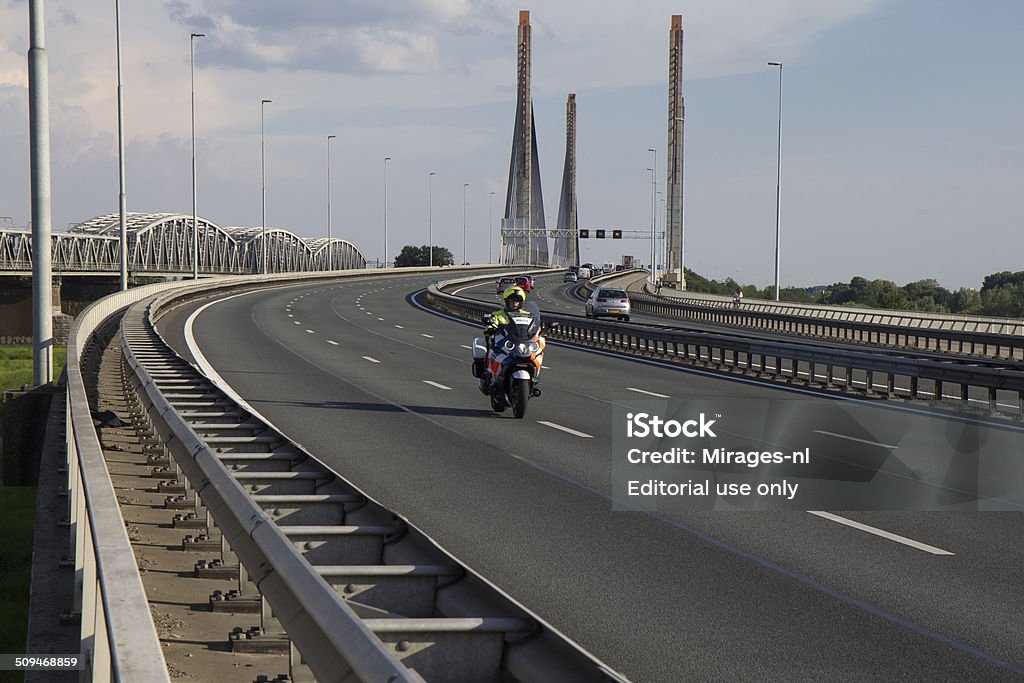 Dutch police man riding a motorcycle on a highway bridge. Zaltbommel, The Netherlands - July 24, 2014: A Dutch police man riding a motorcycle across the Martinus Nijhoff bridge near Zaltbommel. Bridge - Built Structure Stock Photo