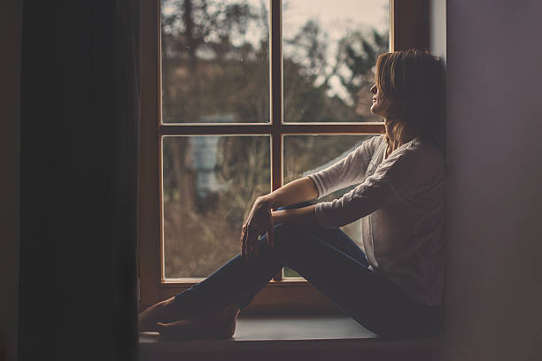 istock Young attractive woman, sitting on a window, looking outside 509471474