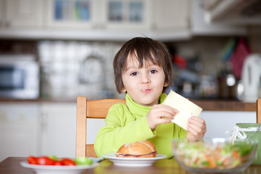 Beautiful little boy, eating sandwich at home, vegetables on the table