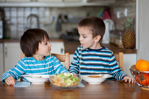 Two sweet children, boy brothers, having for lunch spaghetti at home, enjoying tasty food