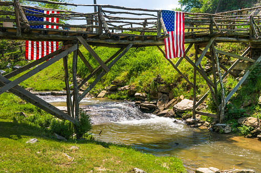 A rustic footbridge with American flags hanging from both sides crosses a creek in  rural Tennessee