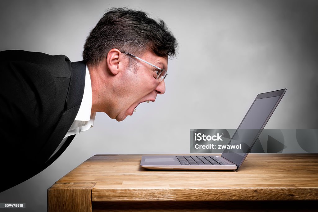 Man screaming at laptop Man sitting at the table and screaming at his laptop Computer Stock Photo