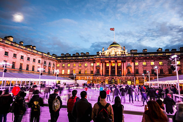 Spectators watching People Ice Skating at Somerset House, London London, UK - December 21, 2015: Blurred motion of crowds of people ice skating at Somerset House, a publically owned building in central London. The image features warm evening light, and an ominous, moody sky. The people appear as unrecognisable blurs due to the long exposure used. Somerset House is a large Neoclassical building situated on the south side of the Strand in central London, overlooking the River Thames, just east of Waterloo Bridge. long exposure winter crowd blurred motion stock pictures, royalty-free photos & images
