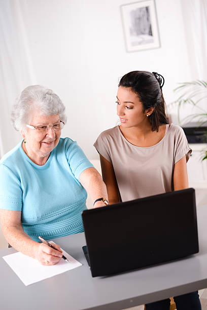 istock cheerful young woman teaching computer and internet to elderly person 509488985